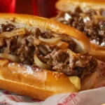 Lifestyle shot of Philly cheesesteaks served on a dining table with fries and condiments, representing the full experience of enjoying a classic Philly cheesesteak.