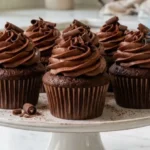 Moist homemade chocolate cupcakes with chocolate buttercream frosting on a white marble countertop.