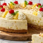 Four-Ingredient Pineapple No-Bake Cheesecake topped with whipped cream, pineapple chunks and toasted coconut on a white marble countertop.