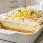 Million Dollar Pineapple Dessert served in a white baking dish with whipped cream, toasted coconut and pineapple.