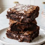 Three-Ingredient Brownies stacked on a white plate with fudgy centers and shiny crackly tops.