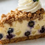 Bakery-style Pineapple Blueberry Crumble Cheesecake on a white cake stand with fresh blueberries and pineapple.