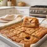 Caramel apple blondies square lifted on a dessert fork from a parchment-lined pan with caramel drizzle on white marble